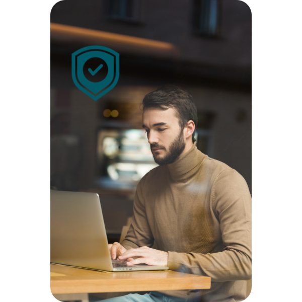 Enhanced Security for Your Finances A Man Wearing A Brown Turtleneck Sitting At A Wooden Table Using A Laptop, With A Security Shield Icon And Checkmark Symbolizing Safety And Reliability