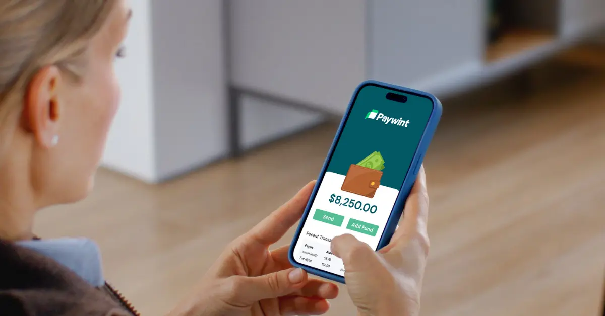 A Person Holds a Smartphone Displaying the Paywint App with a Balance of $8,250, Set in a Cozy Indoor Environment
