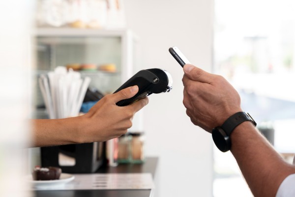 A Customer Is Using a Mobile Phone to Make a Payment at a Cafe, While the Staff Holds a Card Reader