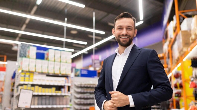 A Man in a Suit Stands Confidently in a Brightly Lit Store Aisle Filled with Various Products and Supplies